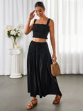 Woman in a black smocked crop top and maxi skirt with hand on forehead