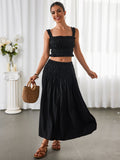 Woman in a black smocked crop top and maxi skirt holding a straw bag