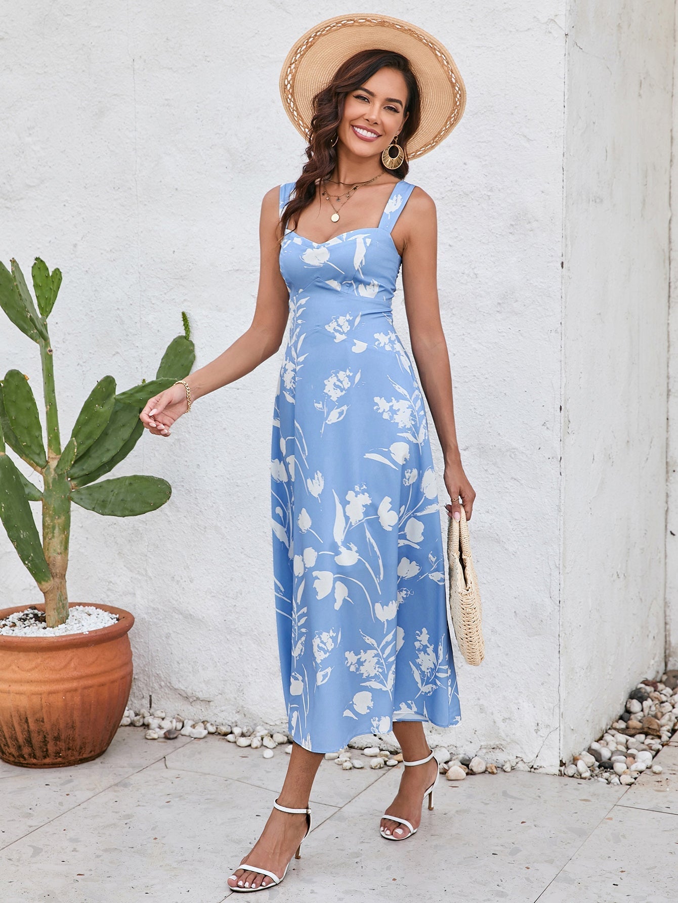 Woman posing with a straw hat and a straw handbag, wearing a blue floral print midi dress.