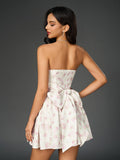 Back view of a woman in a strapless floral print mini dress with a ruched bodice and a bow detail.