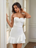 Woman adjusting earring while wearing a white strapless ruched bodice sheath dress with an asymmetrical ruffle hem.