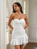 Front view of a woman in a white strapless ruched bodice sheath dress with an asymmetrical ruffle hem.
