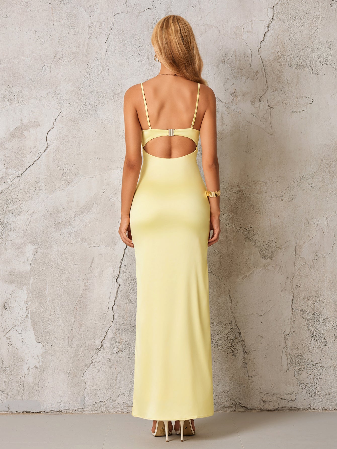 Back view of a woman in a pale yellow satin formal gown, showcasing an open back with a clasp detail and floor-length hem.