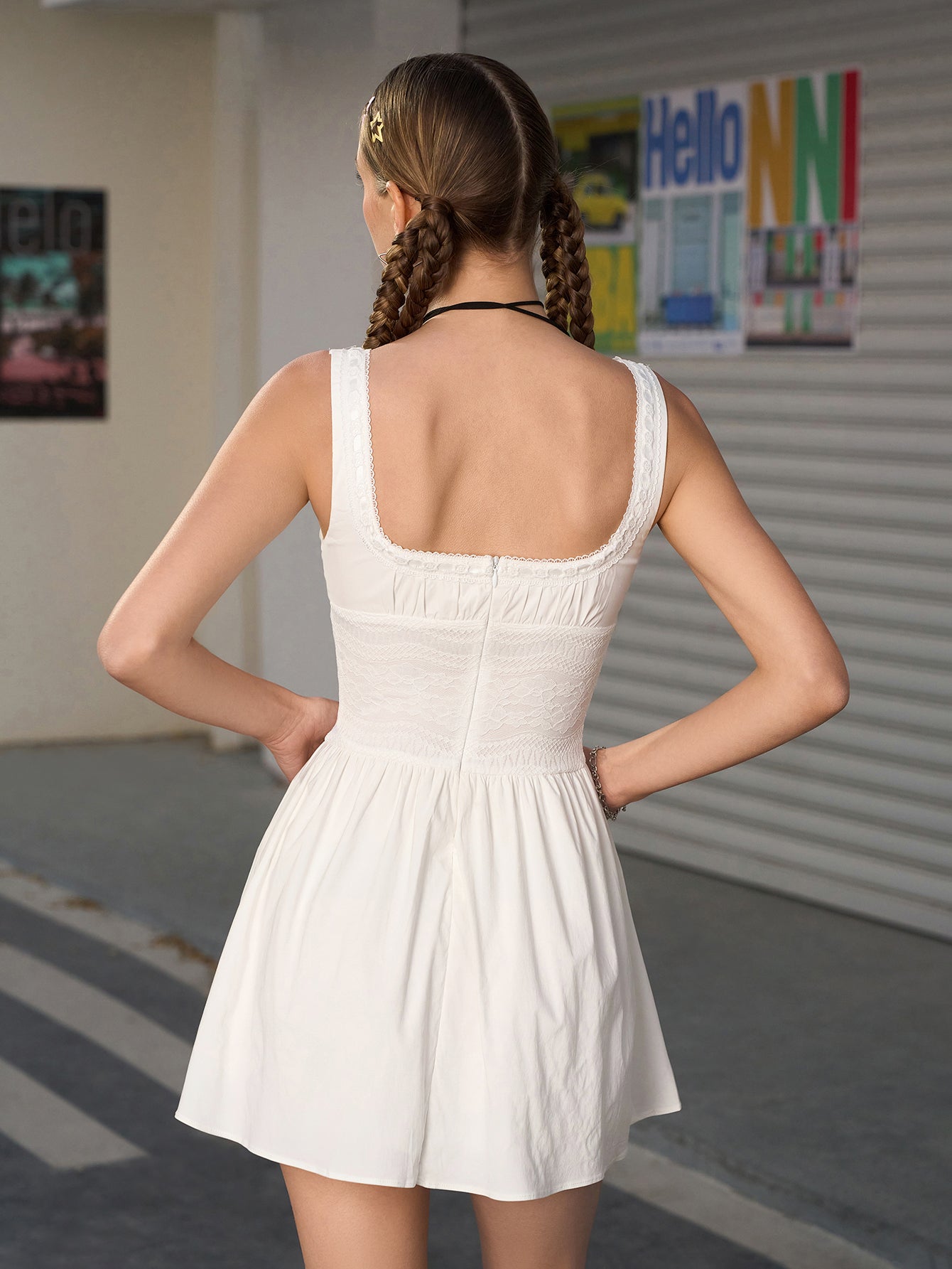 Back view of a woman in a white sleeveless mini dress with a square neckline and lace trim
