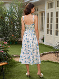 Back view of a woman in a white floral print midi dress with blue flowers, featuring adjustable spaghetti straps and a corset-style lace-up back, standing in a garden.