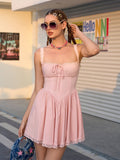 Woman in a pink mini dress with lace trim and a tie front, posing outdoors.