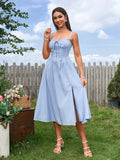 Full body shot of a woman in a light blue midi dress with a slit, outdoors.