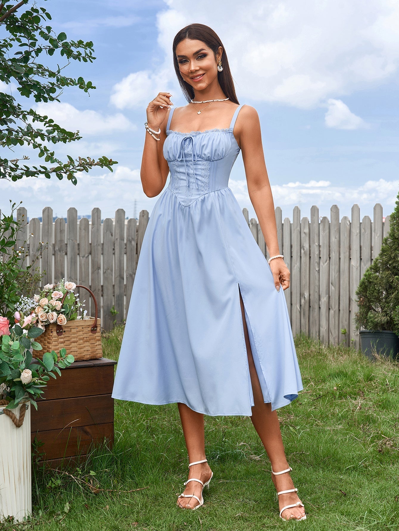 Full body shot of a woman in a light blue midi dress with a slit, outdoors.