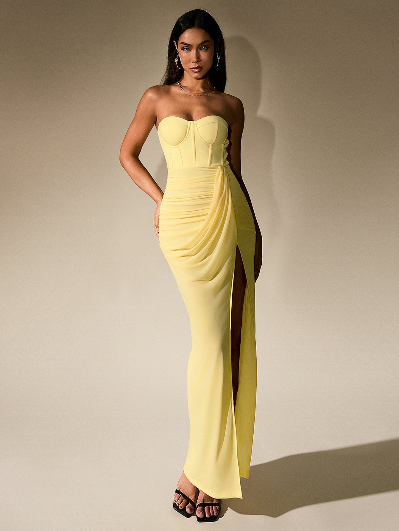 Full-length shot of a woman in a yellow ruched chiffon gown with a thigh-high slit.