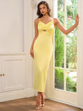 Full-length shot of a woman in a yellow satin sheath dress with spaghetti straps, by a window.