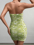 Back view of a woman in a green and white abstract print strapless ruched bodycon mini dress.