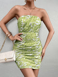 Woman in a green and white abstract print strapless ruched bodycon mini dress, with a white clutch and jewelry.