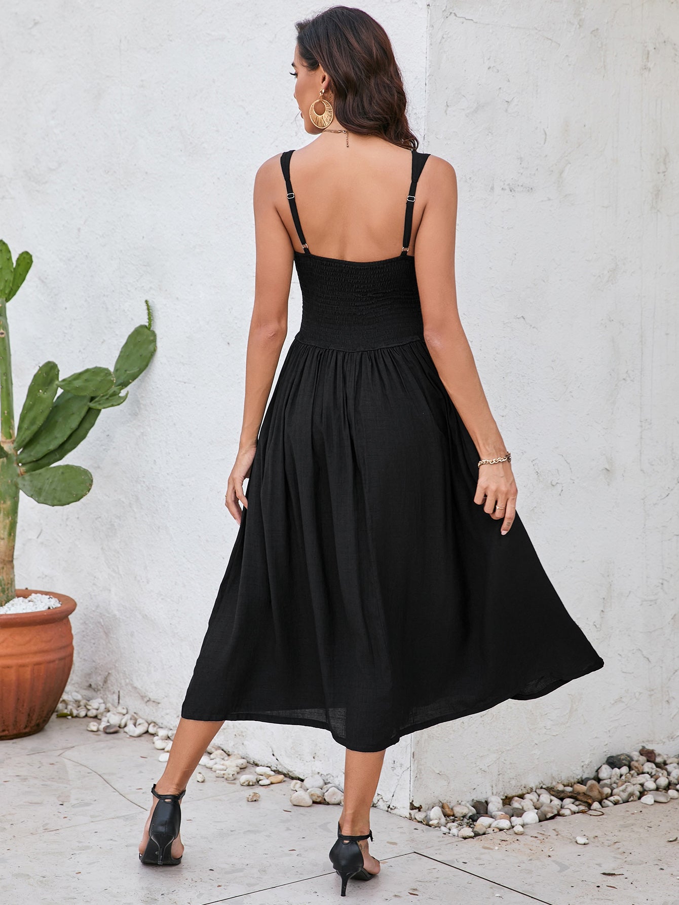 Back view of a woman in a black sleeveless midi dress with a smocked bodice and full skirt.