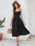 Woman wearing a black sleeveless midi dress with a smocked bodice and full skirt, holding a straw bag and wearing a straw hat.