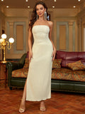 Full length shot of a woman wearing a cream strapless column maxi dress with a ruched bodice and high slit.