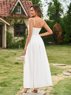 Rear view of a woman in a white maxi dress with spaghetti straps and a smocked back, standing in a garden.