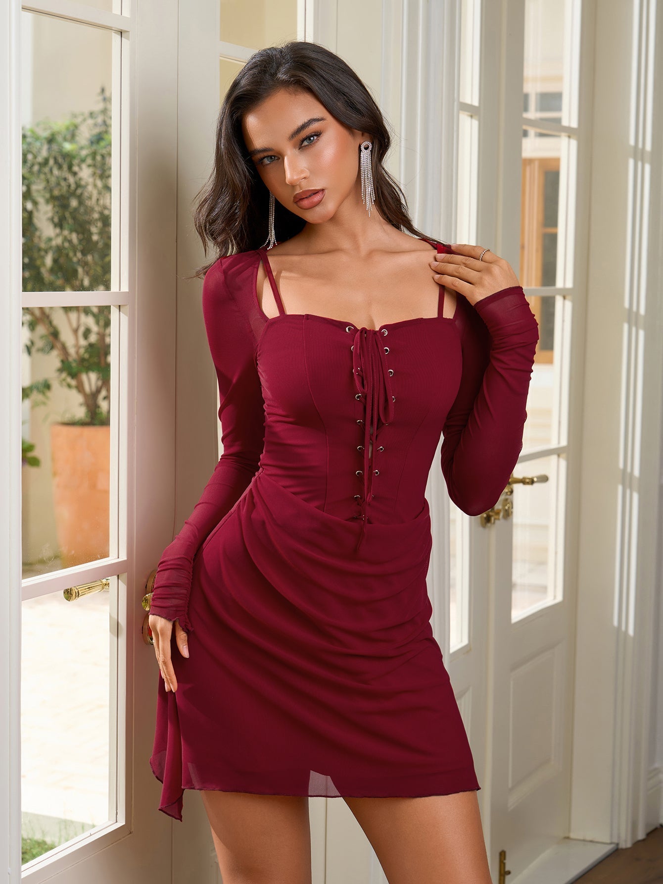 Close-up of a woman in a burgundy long-sleeved dress with a lace-up front and square neckline.