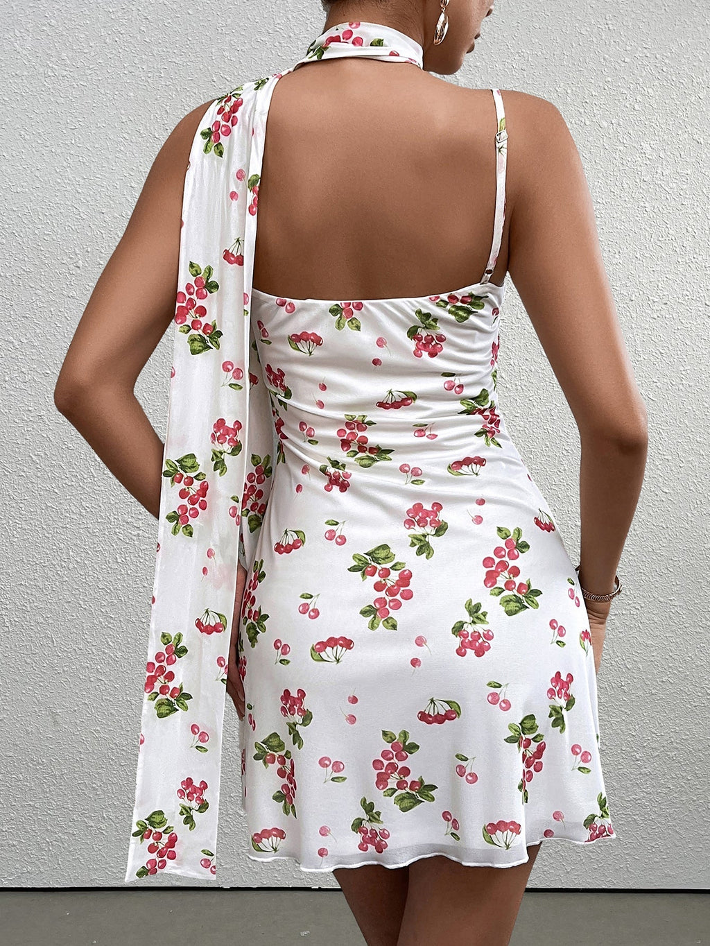 back view of a woman in a white sleeveless A-line dress with a red cherry print and a matching scarf
