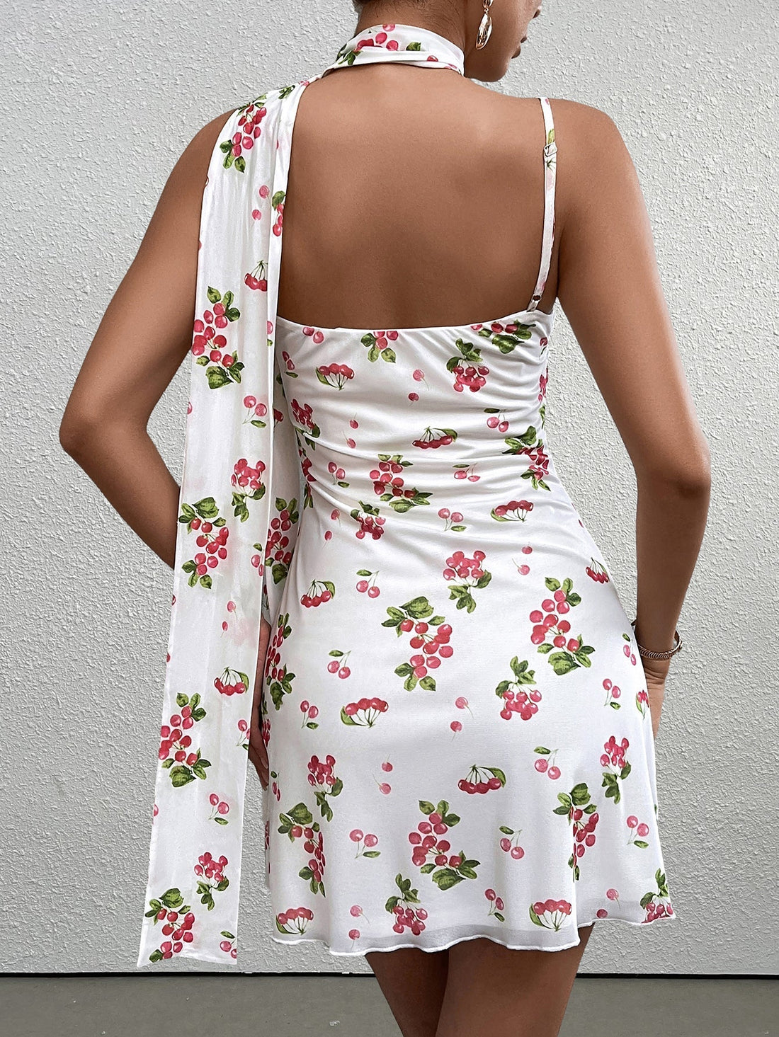 woman wearing a white sleeveless A-line dress with a red cherry print and a knot front detail