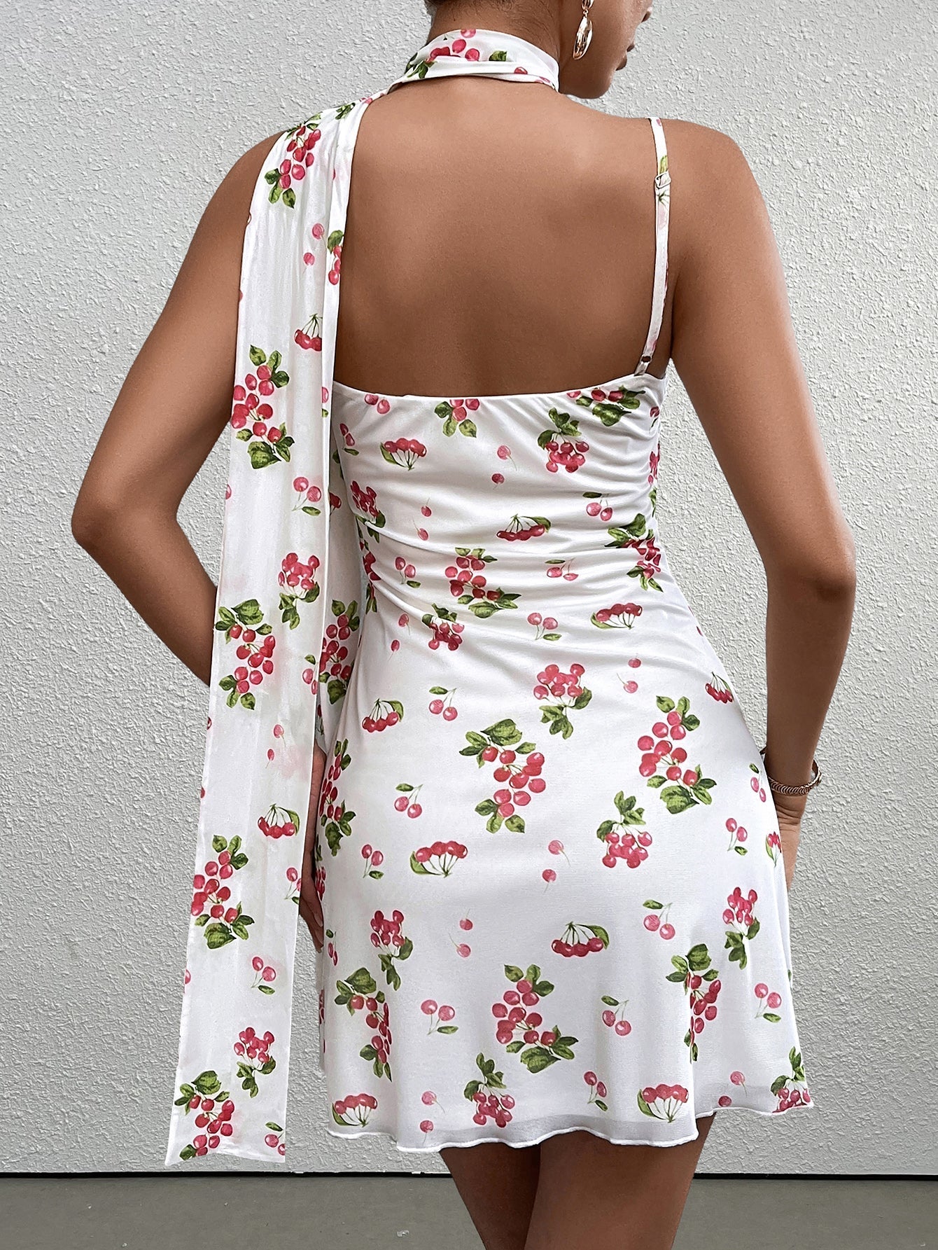 back view of a woman in a white sleeveless A-line dress with a red cherry print and a matching scarf