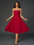Woman wearing a red strapless midi dress with a ruched bodice and full skirt, posing with arms outstretched