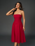 Woman in a red strapless midi dress with a ruched bodice and full skirt, touching her neck