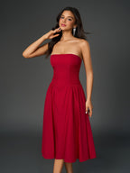 Woman in a red strapless midi dress with a ruched bodice and full skirt, touching her neck