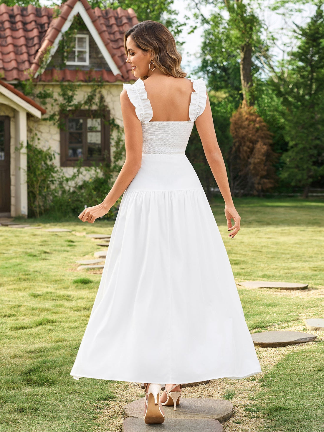 Woman wearing a white sleeveless midi dress with ruffled shoulder straps and a smocked bodice, standing in a garden.