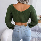 Back view of a woman wearing a green knit cropped sweater with an open back and V-neck.