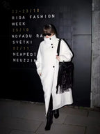 Woman in a white wool blend coat standing in front of a black sign with text
