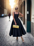 Woman wearing a black sleeveless midi dress with a square neckline and full A-line skirt.