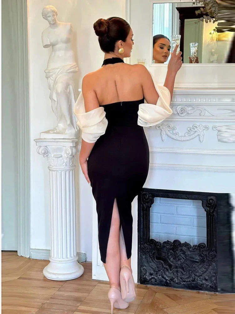 A woman standing in a classic pose with one hand on her hip, wearing an off-the-shoulder black dress with a 3D flower design, paired with white platform heels and a white belt.