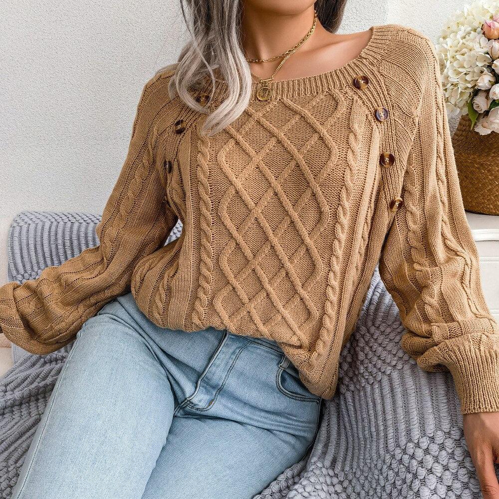 Woman sitting and wearing a tan cable knit sweater with a square neckline and decorative buttons.