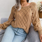 Woman sitting and wearing a tan cable knit sweater with a square neckline and decorative buttons.