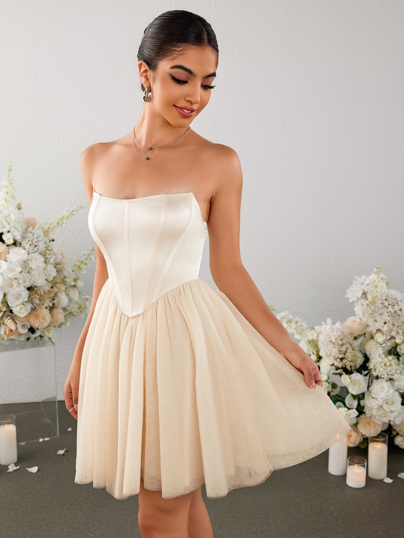 Woman in an ivory strapless corset bodice mini dress with a tulle skirt, looking down and holding the skirt