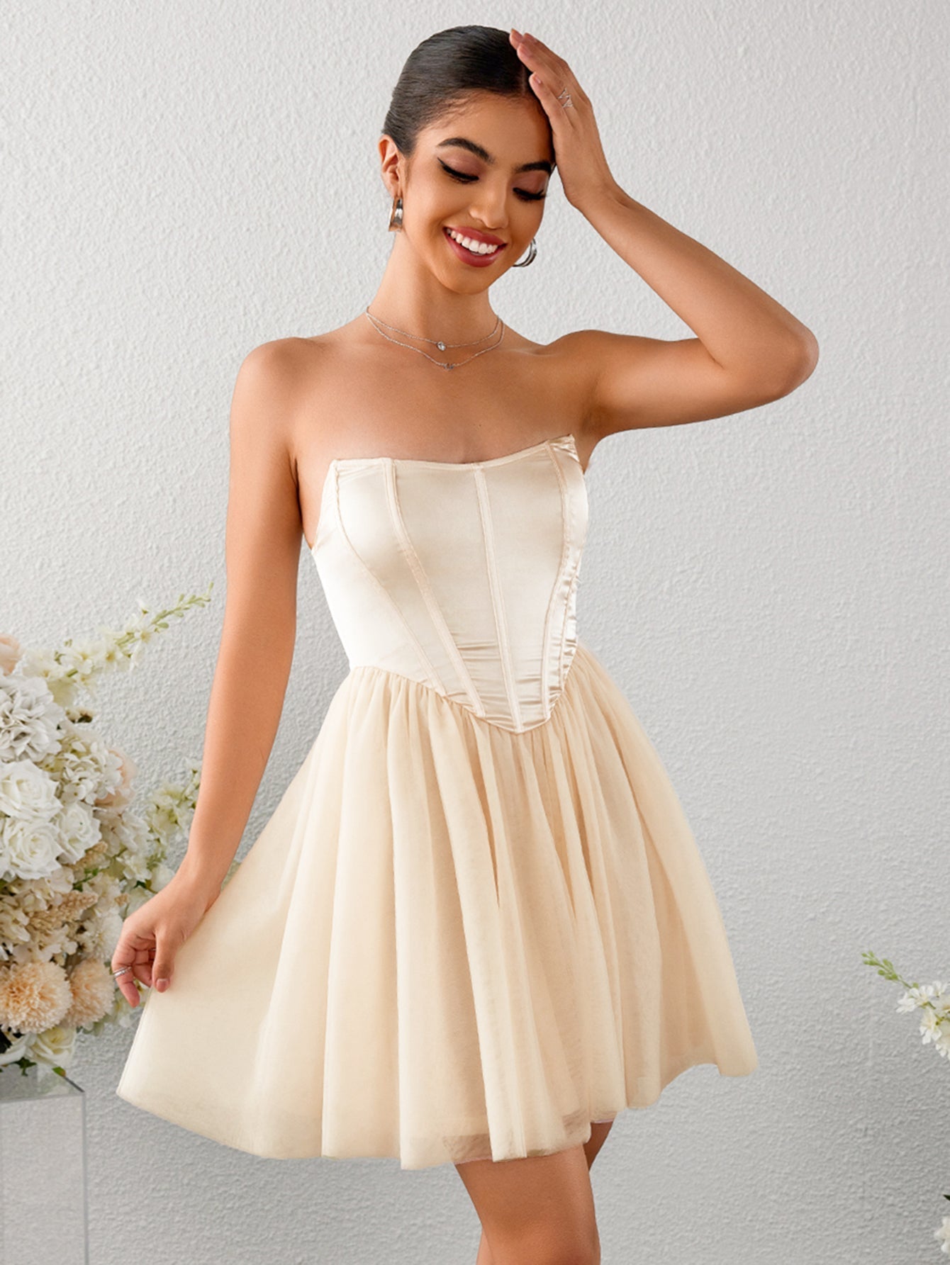 Woman smiling and touching her hair in a strapless ivory satin corset bodice mini dress with a tulle skirt