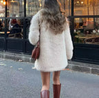 Back view of a woman wearing a cream faux fur coat with a notch lapel and long sleeves.