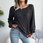 Woman wearing a dark gray cable knit sweater with scoop neckline and button details, paired with light wash jeans.