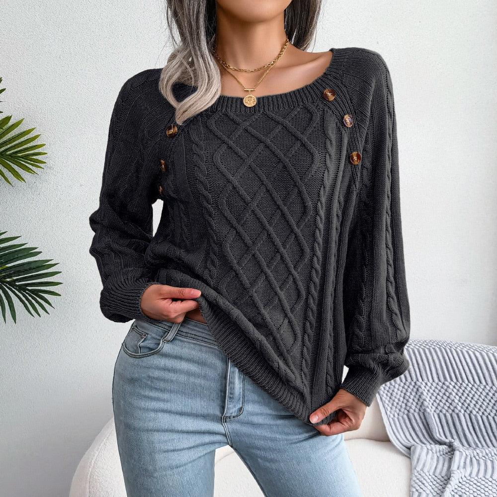 Woman wearing a dark gray cable knit sweater with scoop neckline and button details, paired with light wash jeans.