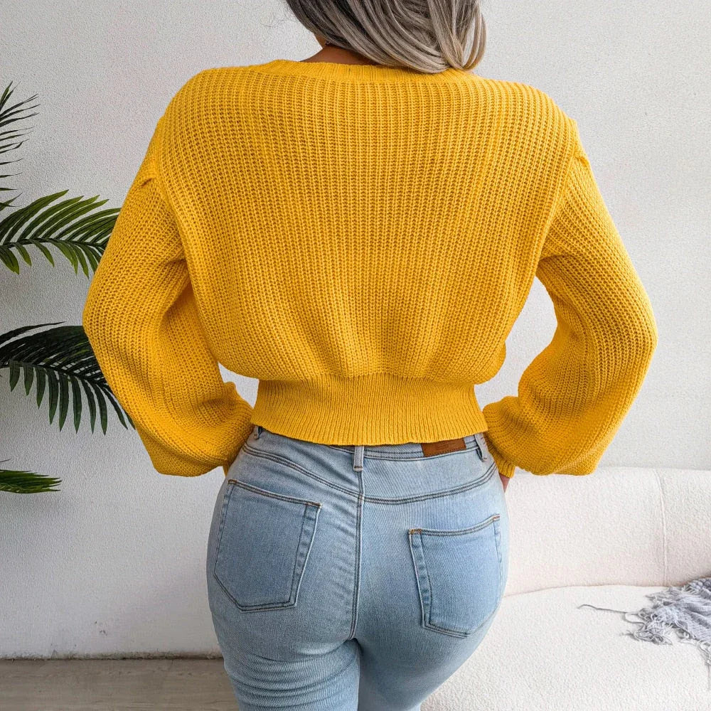Back view of a woman in a yellow cable knit cropped sweater paired with blue jeans.