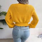 Back view of a woman in a yellow cable knit cropped sweater paired with blue jeans.