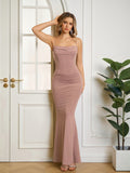 Woman wearing a long, taupe, spaghetti strap, ruched mermaid dress with a cowl neckline, touching her hair.