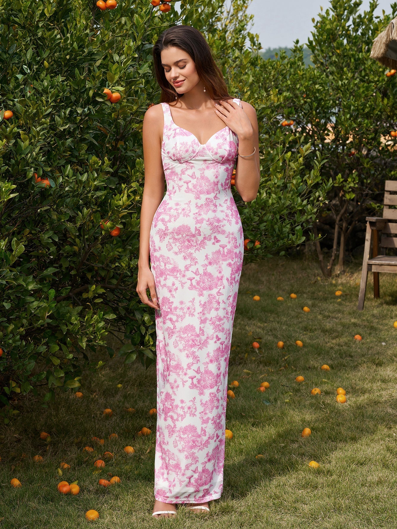 Front view of a woman in a long white and pink floral print column dress with tank straps and a scoop neckline, posing outdoors.