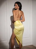 Back view of a woman in a yellow satin bodycon dress with a high slit and a backless design with crisscross straps.
