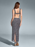 Back view of a woman in a floor-length silver sequined gown with an open back and a high slit, standing against a grey backdrop.
