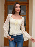 Woman in a cream lace top and blue jeans standing in front of a wooden door