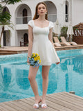 Woman in a white cap sleeve square neck fit and flare dress with a pleated hem detail, holding a bouquet of flowers by a swimming pool.