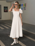 Full body shot of a woman in a white puff sleeve midi dress, adjusting sunglasses.