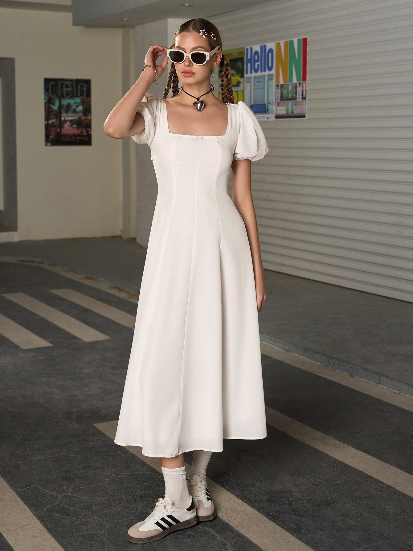 Full body shot of a woman in a white puff sleeve midi dress, adjusting sunglasses.
