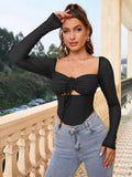 Woman in a black long-sleeve cropped top with a square neckline and tie detail, touching her hair.